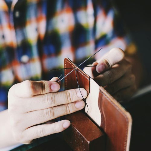 Close-up of a person hand-stitching leather, showcasing detailed craftsmanship and DIY skills.